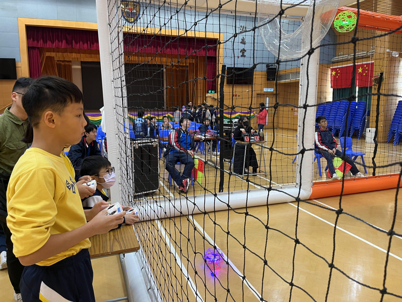 A young pilot using a controller beside a netted drone soccer playing area