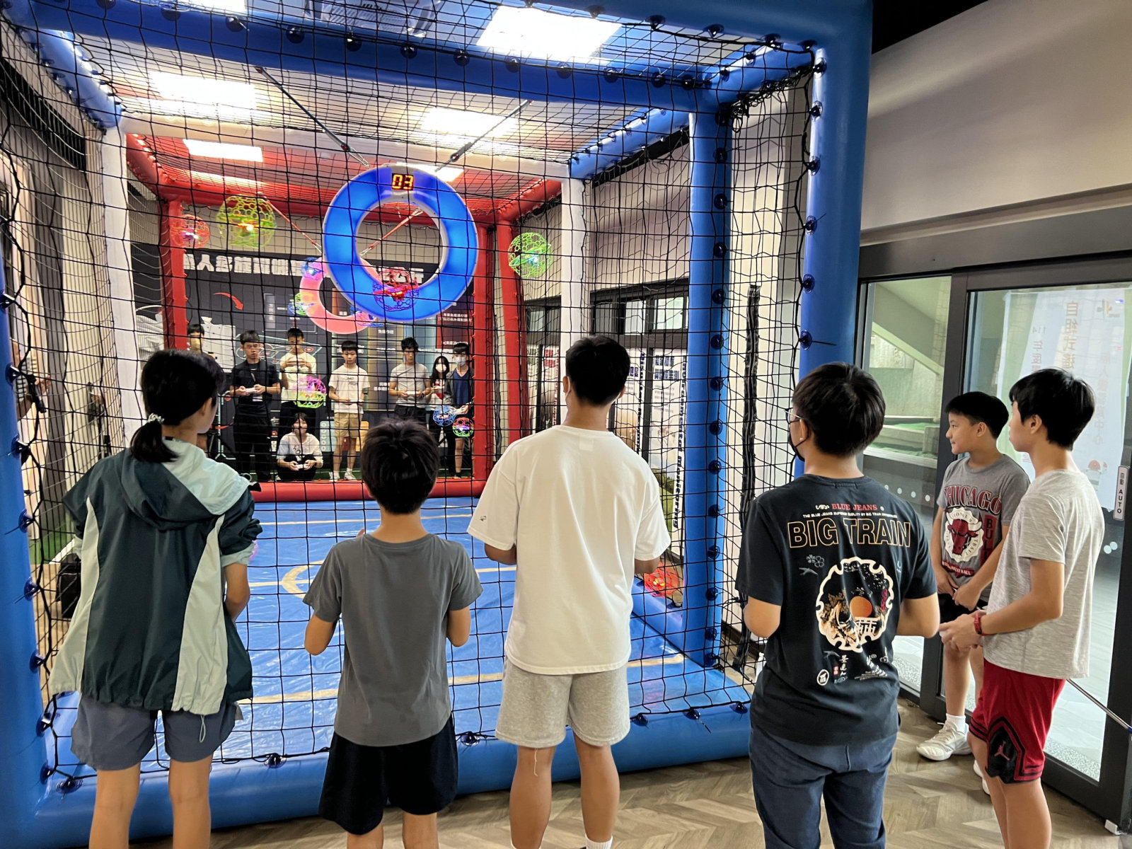 Young participants observing drone soccer inside a netted arena