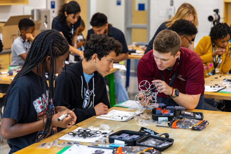 Students and an instructor examining drone components at a workbench